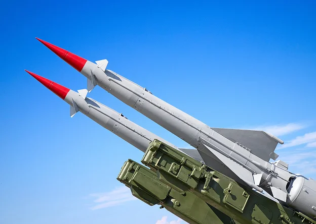 Deux missiles gris à têtes rouges pointent vers un ciel bleu clair.