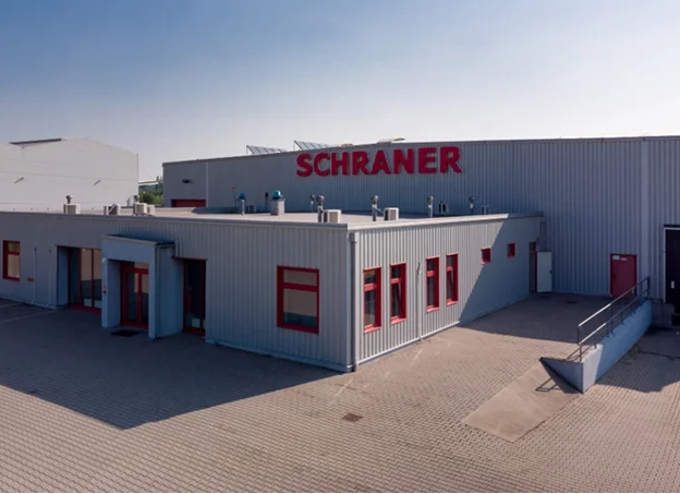 Bâtiment industriel gris avec des accents rouges et l'enseigne SCHRANER.